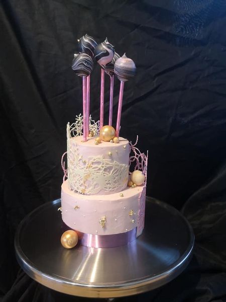 Pink ganache cake with pink chocolate lace and swirled chocolate cake pops and gold balls
